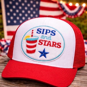 Puede incluir: Gorra de camionero roja y blanca con visera roja y parte trasera de malla. La gorra presenta un parche circular con el texto "SIPS and STARS" y un gráfico de una bebida con una rodaja de limón y una estrella azul.