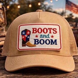May include: Tan trucker hat with a mesh back and a rectangular patch. The patch features a cowboy boot design with red, white, and blue stars and stripes, and the words "BOOTS and BOOM" in red and blue.