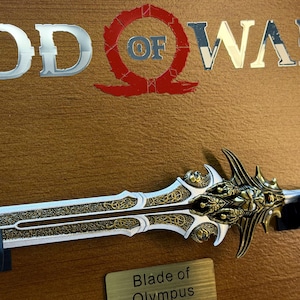 May include: A detailed image of the Blade of Olympus, a prop from the God of War video game. The sword features a gold and silver design with intricate patterns. The God of War logo is visible in the background.