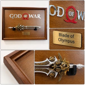 May include: A framed display featuring a replica of the "Blade of Olympus" from the "God of War" video game. The sword is silver and gold, mounted on a wooden plaque with the game's logo and a nameplate.