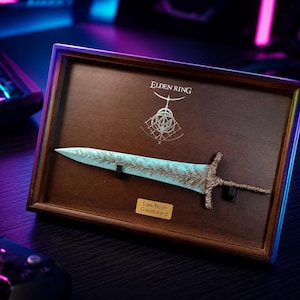 Könnte beinhalten: Gerahmtes Dark Moon Greatsword aus Elden Ring. Das Schwert hat eine blaue Klinge mit detailliertem Design und einen braunen Griff. Der Holzrahmen zeigt das Spiel-Logo und einen Text auf einem kleinen Schild.