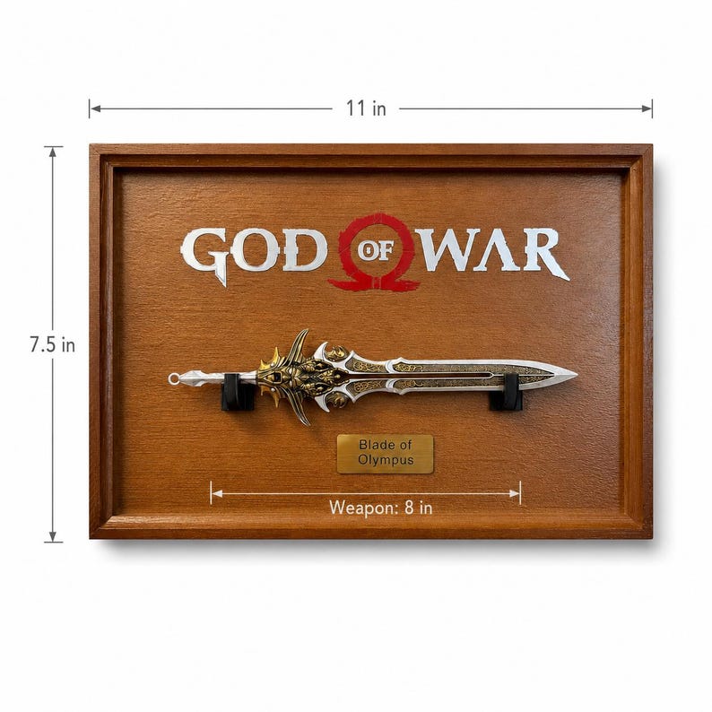 May include: A framed wooden display featuring the "God of War" logo and a replica of the "Blade of Olympus." The sword is 8 inches long, with intricate gold and silver detailing. The frame is 11 inches wide and 7.5 inches tall.