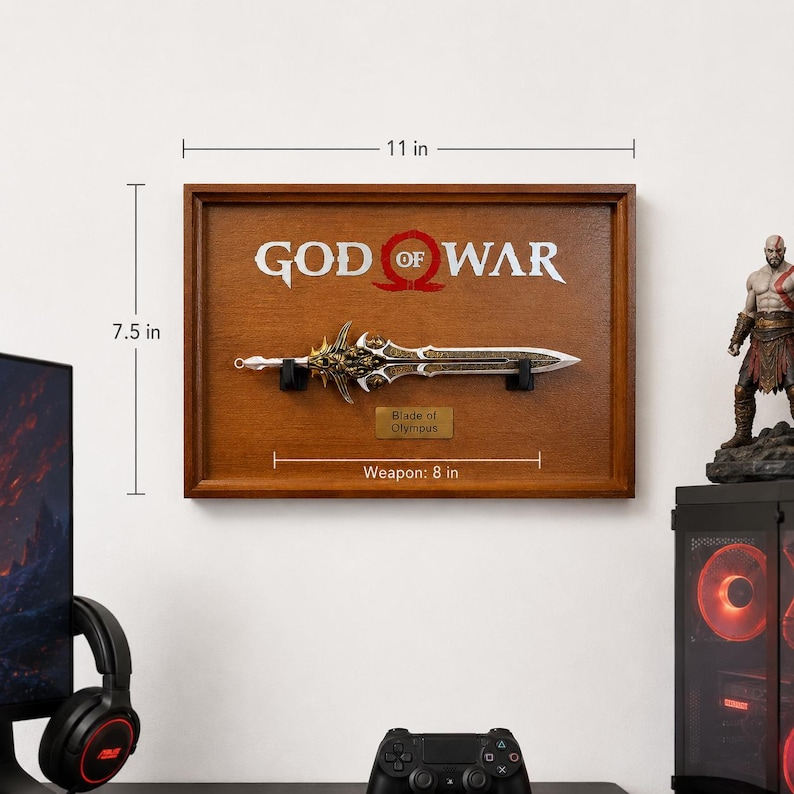 May include: A framed wooden display featuring a replica of the "Blade of Olympus" from the "God of War" video game. The sword is 8 inches long and mounted on a brown wooden plaque that is 11 inches wide and 7.5 inches tall. The words "GOD OF WAR" are displayed above the sword.