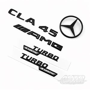 May include: Black car emblems including "CLA", "45", "AMG", "TURBO", "4MATIC", and a Mercedes-Benz logo. The emblems are arranged on a white surface. The emblems are likely for a Mercedes-Benz CLA 45 AMG.