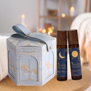 May include: A pale blue hexagonal gift box with a carousel design and a matching ribbon, next to two essential oil roll-on bottles. The bottles have wooden caps and labels with moon and sun graphics.