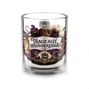 Può includere: Un bicchiere trasparente con una stampa grafica colorata e il testo "TRAGICALLY MISUNDERSTOOD". Il design include un cappello da pirata, un uncino, un orologio da taschino, un telescopio, una mappa e la sagoma di una nave tra fumo viola.