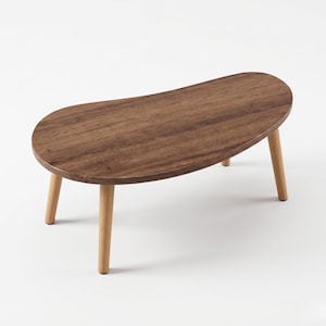 May include: A small, oval-shaped wooden coffee table with a dark brown tabletop and four light-colored wooden legs. The tabletop has a natural wood grain pattern. The table is approximately 36 inches long.
