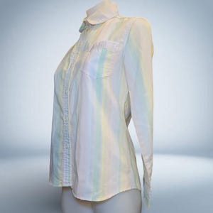 May include: A long-sleeved button-down shirt with a pastel striped pattern in shades of white, yellow, blue, and green. The shirt has a small chest pocket and a rounded collar. The shirt is displayed on a mannequin.