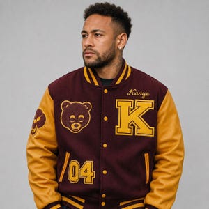 May include: Maroon and gold varsity jacket with the name "Kanye" and a large "K" patch. The jacket features a bear graphic and the number "04". The sleeves are gold, and the body is maroon.