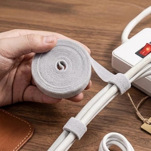 Könnte beinhalten: Nahaufnahme von grauen Kabelbindern und weißen Kabeln. Die Kabel werden mit grauen Kabelbindern aus Samt befestigt. Ein Etikett lautet: "VELVET CABLE WRAPS - ARTISAN QUALITY."