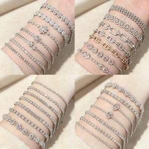 May include: A collection of twenty-four silver and gold-toned metal bracelets featuring various designs, including tennis bracelets with round, marquise, and heart-shaped clear stones, chain-link styles, and delicate bands with small colored accents.