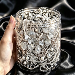 May include: A clear cylindrical plastic jar filled with a collection of silver-toned jewelry, including necklaces with metallic flower-shaped pendants, white faux pearl strands, rhinestone-encrusted star motifs, and teardrop-shaped charms.