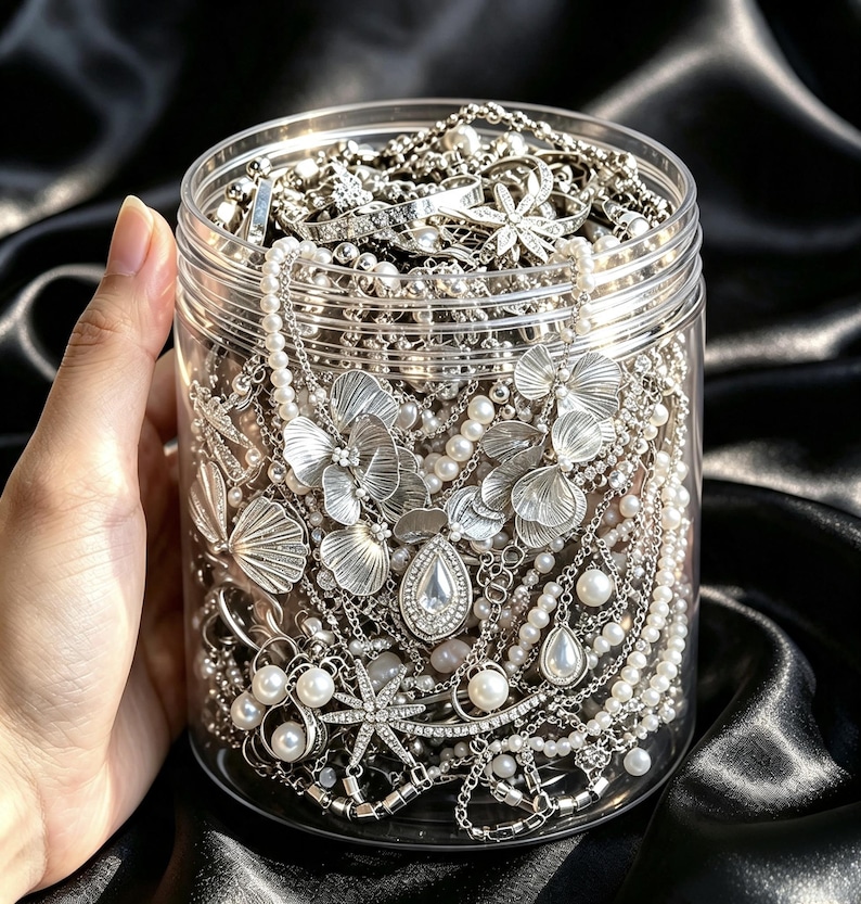May include: A clear cylindrical plastic jar filled with a collection of silver-toned jewelry, including necklaces with metallic flower-shaped pendants, white faux pearl strands, rhinestone-encrusted star motifs, and teardrop-shaped charms.