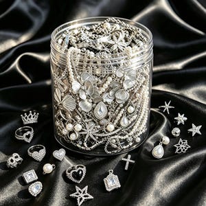 May include: A clear plastic jar filled with silver-toned jewelry, including necklaces with floral and teardrop pendants, pearl strands, and chains. Scattered around the jar are various silver rings, star-shaped charms, a cross, and pearl earrings.