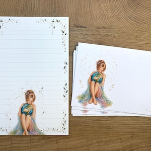 Könnte beinhalten: Briefpapier-Set mit einem linierten Briefbogen und mehreren leeren Karten. Jedes Stück hat einen dekorativen Rand und eine Aquarellillustration einer Person, die einen Globus hält. Die Illustration ist in Pastellfarben gehalten.