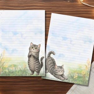 Könnte beinhalten: Zwei Blatt liniertes Briefpapier mit Aquarellillustrationen einer grauen getigerten Katze. Ein Blatt zeigt die Katze aufrecht stehend, während das andere die Katze beim Strecken zeigt. Der Hintergrund zeigt einen blauen Himmel und grünes Gras.