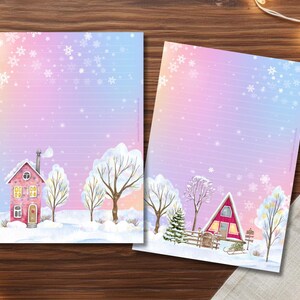 Könnte beinhalten: Zwei Briefpapierbögen mit einer Winterszene. Das Papier hat einen Farbverlaufshintergrund aus Rosa, Lila und Blau mit Schneeflocken. Ein Bogen zeigt ein rosa Haus, der andere eine rote A-Frame-Hütte. Beide haben schneebedeckte Bäume.