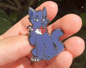 Op de afbeelding: Een donkerblauwe emaille speld met een gestileerde kat met puntige oren, een paarse halsband en een witte vlek op de borst. De kat zit in een zittende houding met één poot bij de mond, waarbij scherpe klauwen en een rood accent zichtbaar zijn.