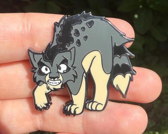 Puede incluir: Un pin de esmalte metálico que representa una criatura de dibujos animados estilizada con pelaje gris y crema, una espalda con rayas negras y una expresión gruñona. El personaje tiene orejas puntiagudas, dientes afilados y postura encorvada.