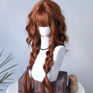 Peut inclure: Une perruque longue et ondulée de couleur auburn, dotée d'une frange droite et de deux sections tressées lâches tombant sur le devant. La perruque est présentée sur une tête de mannequin blanche, mettant en valeur une teinte roux-brun vibrante.