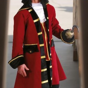 Puede incluir: Un abrigo de disfraz de pirata rojo con detalles en negro y dorado. El abrigo presenta paneles negros con rayas doradas en la parte delantera y en los puños. Un gancho dorado es visible en la mano derecha. El disfraz incluye pantalones negros.