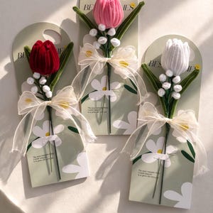 May include: Three decorative tulip flower gifts in red, pink, and white. Each flower is attached to a green stem with white accents and a sheer ribbon bow. The flowers are on a light green card with daisy graphics and the word "BESTIES".