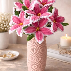 Peut inclure: Un bouquet de fleurs roses avec des bordures blanches et des centres jaunes dans un vase rose. Le vase présente un motif texturé. Des feuilles vertes sont visibles. Une bougie allumée et une petite coupelle sont en arrière-plan.