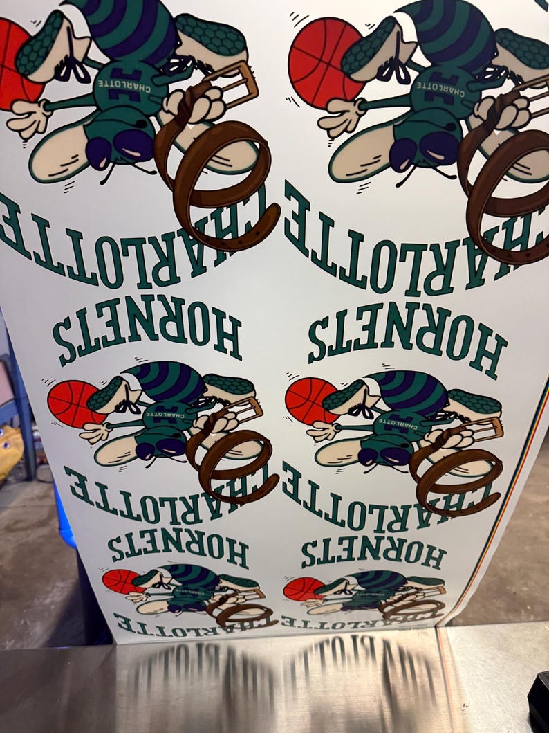 May include: A sheet of paper printed with a repeating pattern featuring the Charlotte Hornets logo. The logo includes a cartoonish bee holding a basketball, with the team name and city name in green text.