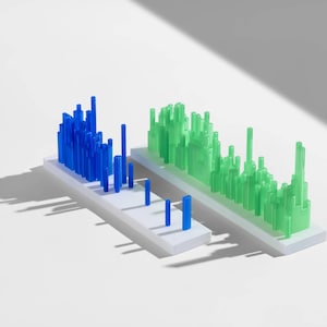 May include: Two abstract sculptures, one blue and one green, each with many vertical rectangular elements. The sculptures are mounted on white rectangular bases. The image is set against a white background with shadows.