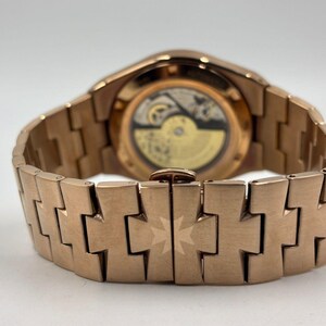 May include: Close-up of a rose gold wristwatch, showcasing the intricate movement through the transparent back. The watch features a matching rose gold bracelet with a distinctive design. The watch is a luxury item.