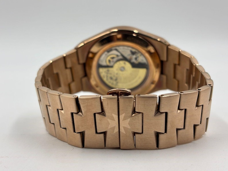 May include: Close-up of a rose gold wristwatch, showcasing the intricate movement through the transparent back. The watch features a matching rose gold bracelet with a distinctive design. The watch is a luxury item.