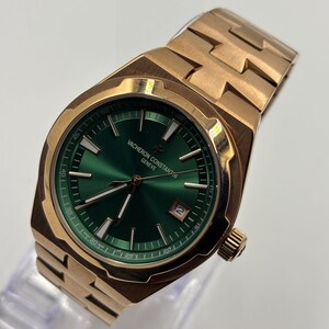 May include: A gold-toned wristwatch with a green face. The watch features a date window and a gold-toned band. The watch face has gold-toned hands and markers. The watch is displayed on a clear stand.