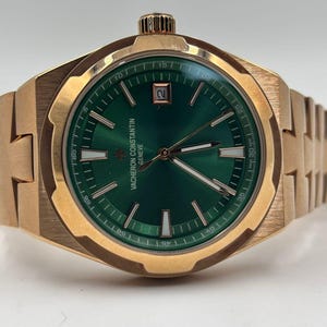 May include: A gold-toned wristwatch with a green dial. The watch features a date window and a textured band. The dial has white markers and hands. The watch is a luxury item.