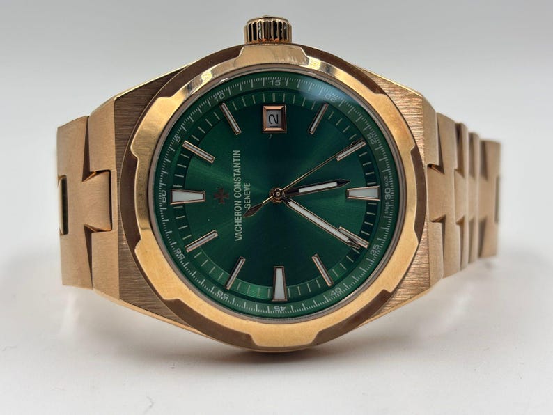 May include: A gold-toned wristwatch with a green dial. The watch features a date window and a textured band. The dial has white markers and hands. The watch is a luxury item.
