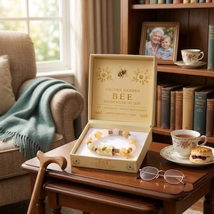 May include: A beaded bracelet with yellow and white stones and a central cylindrical charm featuring a bee illustration, presented in a cream-coloured box with the text Golden Garden Bee Messenger of Joy, Limited Edition 2026 printed inside.