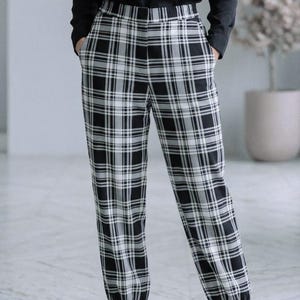 May include: Black and white plaid pants with a jogger style fit. The pants have an elastic waistband and cuffs. The plaid pattern is a classic design, with black and white lines creating a checkered effect. The pants are paired with a black long-sleeve shirt.