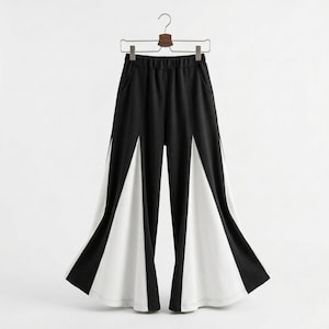 May include: Black and white palazzo pants hanging on a hanger. The pants have a black waistband and upper portion, with white panels extending down the legs. The design creates a striking contrast and a unique, geometric look.
