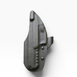 May include: A dark gray, molded polymer holster. The holster has a curved shape with a belt clip and two visible screws. The surface has a textured appearance.