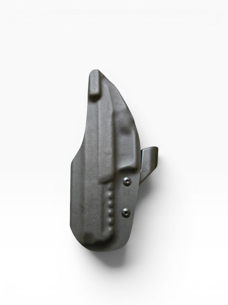 May include: A dark gray, molded polymer holster. The holster has a curved shape with a belt clip and two visible screws. The surface has a textured appearance.