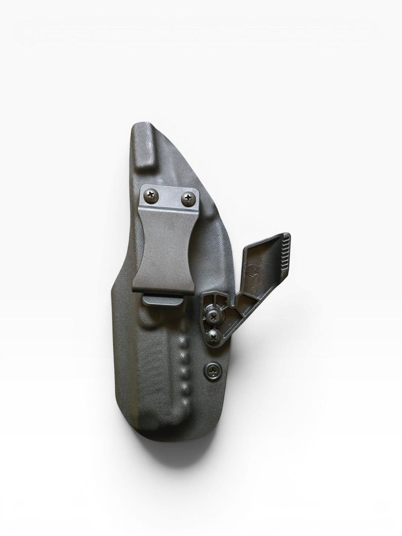 May include: A dark gray, molded polymer holster with a metal belt clip and adjustable retention device. The holster is designed to be worn on the body and has several screws for adjustment and assembly. The overall design is compact and functional.