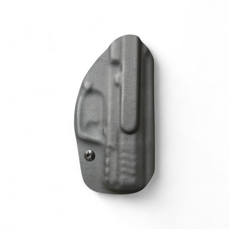 May include: A gray, molded polymer holster with a belt clip. The holster has a textured surface and a small screw. The design is for concealed carry. The holster is shown against a white background.