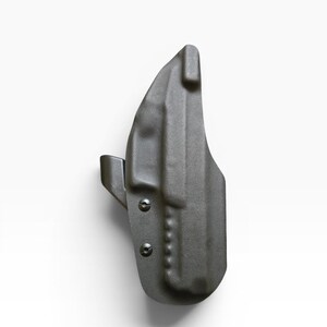 May include: A dark gray, molded polymer holster. The holster features a curved design with a belt clip and is secured with two screws. The overall shape is ergonomic and designed for a firearm.