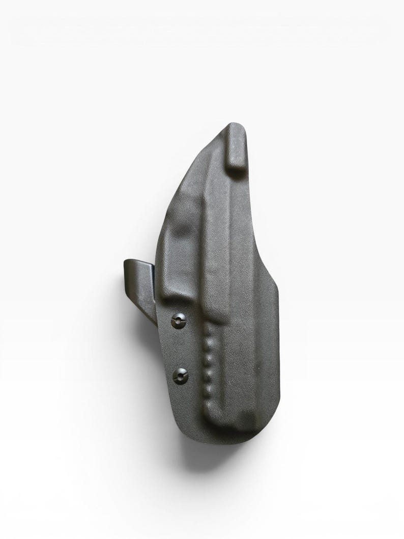 May include: A dark gray, molded polymer holster. The holster features a curved design with a belt clip and is secured with two screws. The overall shape is ergonomic and designed for a firearm.