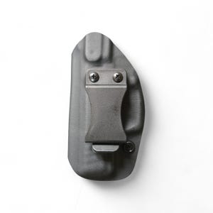 May include: A gray, molded polymer holster with a metal belt clip. The holster is designed to be worn inside the waistband. The clip is secured with two screws. The overall design is minimalist and functional.