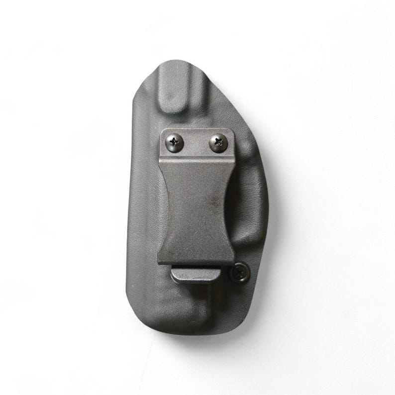 May include: A gray, molded polymer holster with a metal belt clip. The holster is designed to be worn inside the waistband. The clip is secured with two screws. The overall design is minimalist and functional.