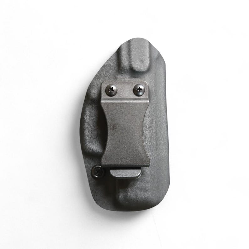 May include: A black, molded polymer holster with a metal belt clip attached with two screws. The holster is designed to be worn on the body. The clip is a dark gray color.