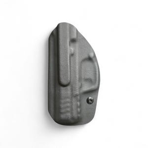 May include: A gray, molded polymer holster with a belt clip and a single screw. The holster is designed to be worn on the body. The surface has a textured finish.