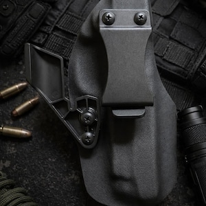 May include: A black polymer holster with a belt clip, secured by screws. The holster is shown with ammunition, tactical gear, and a flashlight. The overall theme suggests tactical or self-defense equipment.