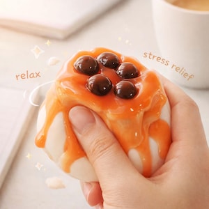 May include: A white and orange stress relief toy shaped like a pastry, topped with brown spheres. The toy is being squeezed by a hand. The words "relax" and "stress relief" are visible.