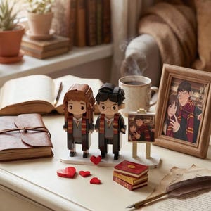 May include: A decorative scene featuring brick-built figures of a couple, small red hearts, and miniature books. A framed photo and a cup of coffee are also present. The figures are wearing scarves and robes.